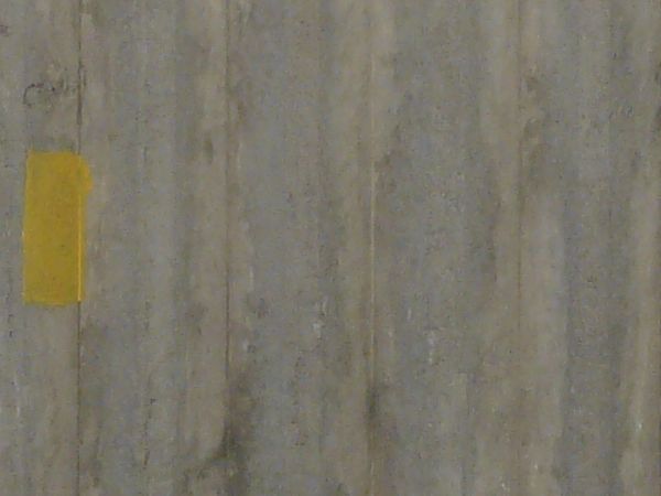 Concrete fence texture molded with a pattern of circles above vertical recessions, with large cracks and stains. The fence appears to be crumbling around the edges.